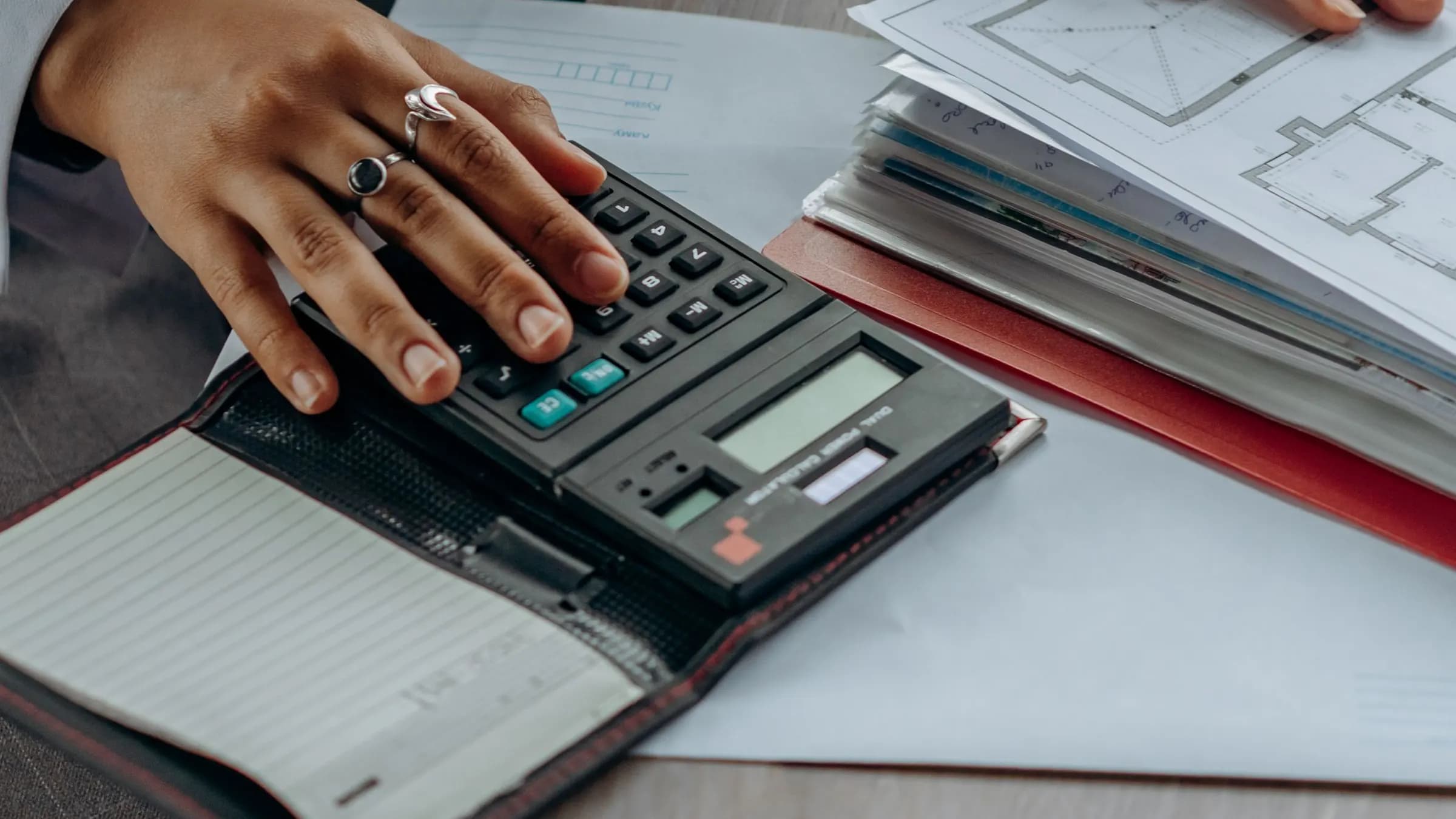An accounts clerk adding up figures on a calculator beside a pile of paperwork.
