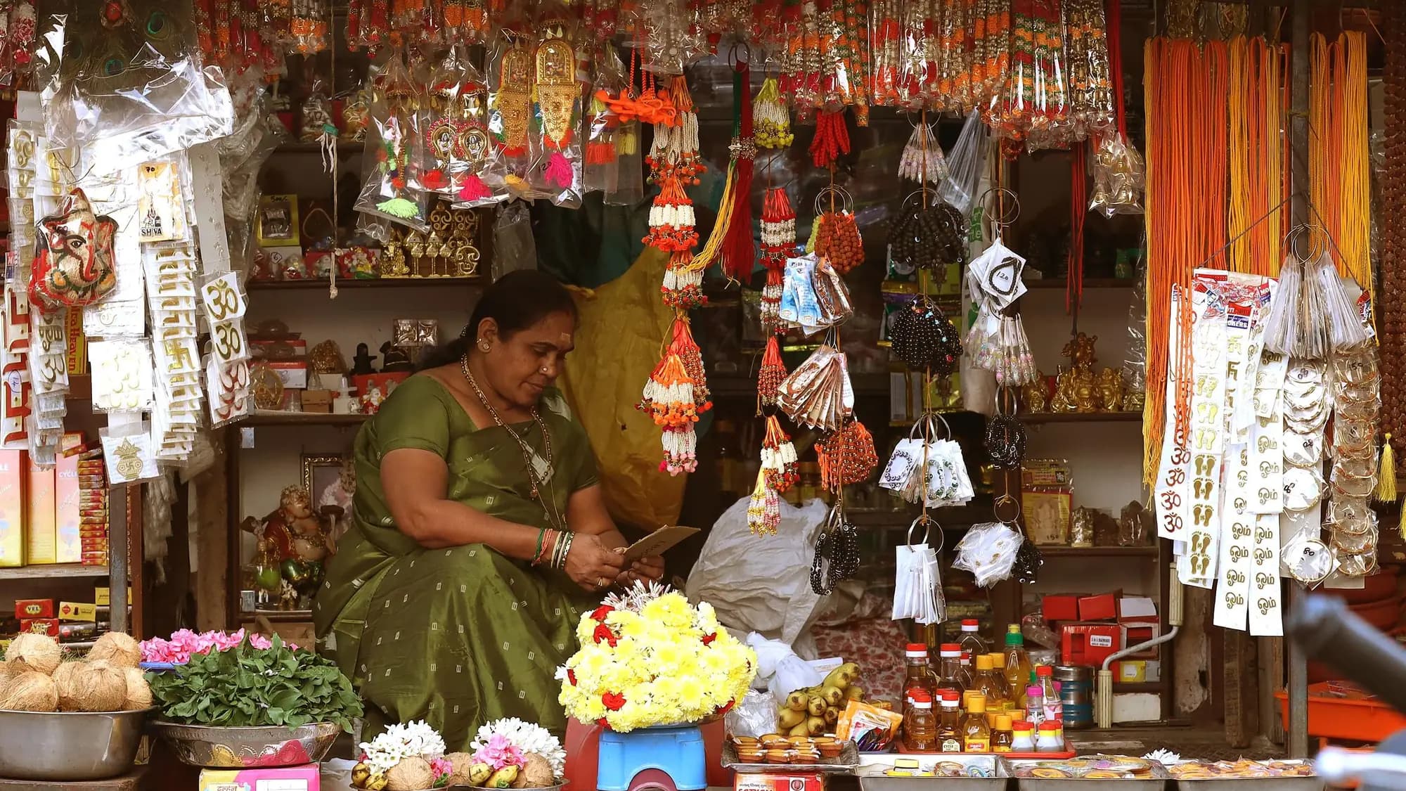 A shopkeeper at her stall in a market in Chennai, surrounded by goods on display.